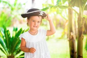 bellissimo poco ragazza nel pirata cappello con un' cranio Tenere un' stella marina su il spiaggia foto