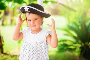 bellissimo poco ragazza nel pirata cappello con un' cranio Tenere un' stella marina su il spiaggia foto