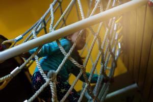 attivo poco bambino giocando su arrampicata netto e salto su trampolino a scuola cortile terreno di gioco. bambini giocare e scalata all'aperto su soleggiato estate giorno. carino ragazza su nido swing a prescolastico sport centro. foto