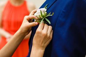 vicino su della sposa mani pinning boutonniere per sposo' giacca foto