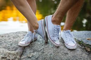 amore storia detto di stivali. umano piedi vicino su. uomo e donna nel scarpe da ginnastica. ragazza nel bianca scarpe. tipo nel nero scarpe da ginnastica e denim. fricchettone coppia nel estate. gambe vicino su. foto