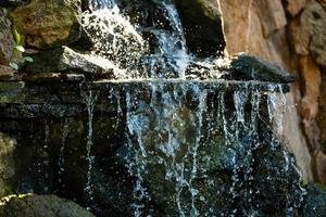 vicino su di acqua spruzzi su rocce a partire dal un' cascata acqua su decorativo pietre foto