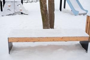 innevato vuoto panchina su il strada, su il terreno di gioco foto