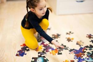 ragazza collegamento sega puzzle pezzi nel un' bambini camera su pavimento a casa. divertimento famiglia attività tempo libero. foto