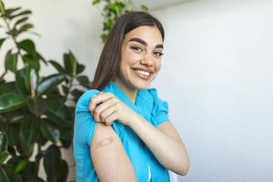 donna puntamento a il suo braccio con un' bendare dopo ricevente il covid-19 vaccino. giovane donna mostrando sua spalla dopo ottenere coronavirus vaccino foto