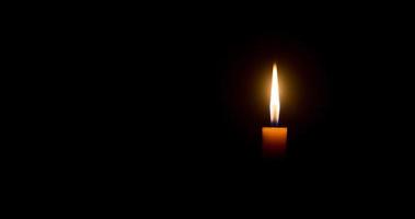 un' singolo ardente candela fiamma o leggero raggiante su un arancia candela su nero o buio sfondo su tavolo nel Chiesa per Natale, funerale o memoriale servizio con copia spazio foto