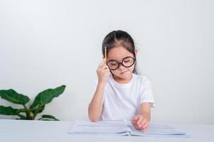 ritratto di poco allievo scrittura a scrivania nel alunno ragazza studia fare test nel primario scuola. bambini scrittura Appunti nel aula. formazione scolastica conoscenza concetto foto