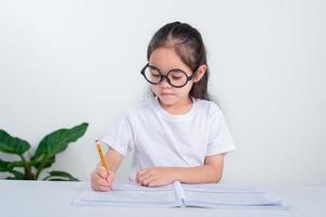 ritratto di poco allievo scrittura a scrivania nel alunno ragazza studia fare test nel primario scuola. bambini scrittura Appunti nel aula. formazione scolastica conoscenza concetto foto