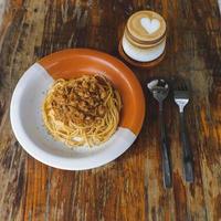 salutare piatto di italiano spaghetti sormontato con un' gustoso pomodoro e terra Manzo bolognese salsa e fresco basilico su un' rustico Marrone di legno tavolo. servito con cappuccino foto