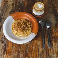 salutare piatto di italiano spaghetti sormontato con un' gustoso pomodoro e terra Manzo bolognese salsa e fresco basilico su un' rustico Marrone di legno tavolo. servito con cappuccino foto