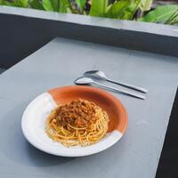 salutare piatto di italiano spaghetti sormontato con un' gustoso pomodoro e terra Manzo bolognese salsa e fresco basilico su un' grigio tavolo. servito con cappuccino foto