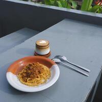 salutare piatto di italiano spaghetti sormontato con un' gustoso pomodoro e terra Manzo bolognese salsa e fresco basilico su un' grigio tavolo. servito con cappuccino foto