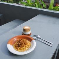 salutare piatto di italiano spaghetti sormontato con un' gustoso pomodoro e terra Manzo bolognese salsa e fresco basilico su un' grigio tavolo. servito con cappuccino foto