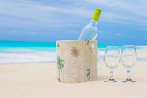 bottiglia di bianca vino e Due bicchieri su il esotico sabbioso spiaggia foto