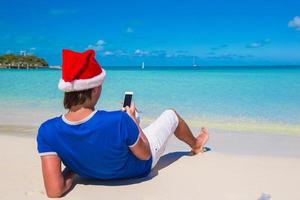 indietro Visualizza di giovane uomo nel Santa cappello con Telefono su tropicale caraibico spiaggia foto