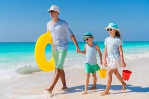 famiglia di papà e bambini a piedi su bianca tropicale spiaggia su caraibico isola con spiaggia giocattoli. famiglia spiaggia vacanze foto