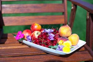 piatto con fresco frutta e fiori su di legno sedie foto