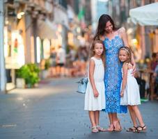 contento madre e poco adorabile ragazze su accogliente strada durante italiano vacanza. famiglia europeo vacanza. foto