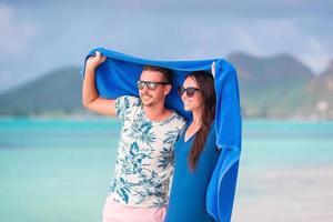 giovane coppia a tropicale spiaggia sotto il asciugamano nascondiglio a partire dal tropicale pioggia. viaggio concetto foto