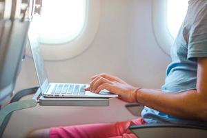 giovane uomo seduta nel il aereo e Lavorando su il suo il computer portatile foto