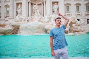 giovane uomo turista trolling monete a trevi Fontana, Roma, Italia per bene fortuna. caucasico tipo fabbricazione un' desiderio per venire Indietro. foto