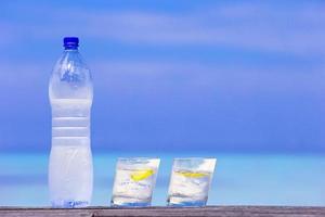 bicchieri di acque con Limone e bottiglia su di legno su mare sfondo foto