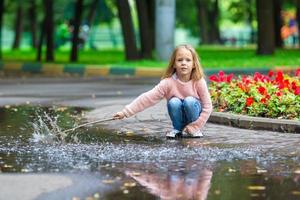 poco contento ragazza avendo divertimento nel un' grande pozzanghera nel autunno parco foto