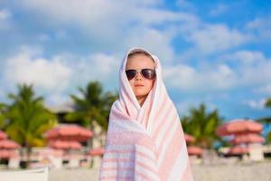 adorabile poco ragazza nel occhiali da sole coperto con asciugamano a tropicale spiaggia foto