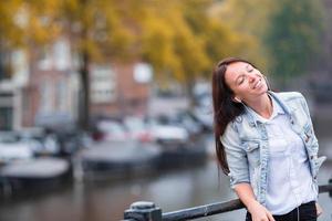 giovane bellissimo donna ascoltando per musica sfondo di canale nel amsterdam, Olanda foto
