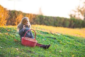 adorabile poco ragazza con un' cestino all'aperto a bellissimo autunno parco foto