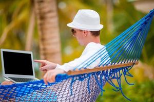 giovane uomo con il computer portatile a amaca su tropicale vacanza foto