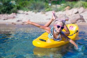 poco ragazza godendo nuoto nel giallo kayak nel il chiaro turchese acqua foto