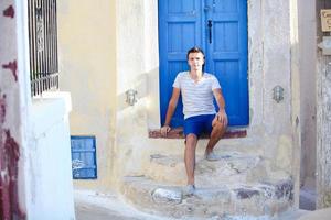 giovane uomo seduta vicino vecchio blu porta di emporio villaggio su il isola Santorini, Grecia foto