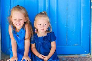 avvicinamento di poco adorabile ragazze seduta vicino vecchio blu porta nel greco villaggio, emporio, santorini foto