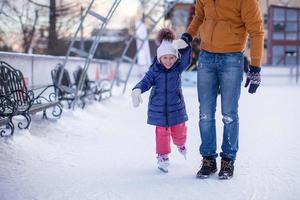 primo piano di adorabile bambina con il giovane papà sulla pista di pattinaggio foto