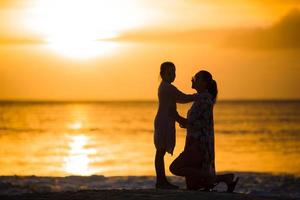 poco ragazza e contento madre silhouette nel il tramonto a il spiaggia foto