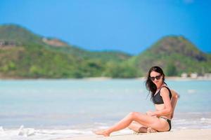 giovane contento donna nel costume da bagno su bianca spiaggia. bellissimo modello nel bikini seduta fuori uso. foto