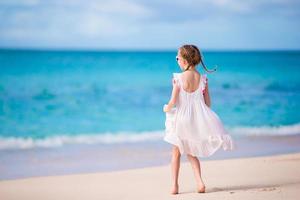 carino poco ragazza nel bianca vestito a spiaggia durante caraibico vacanza foto