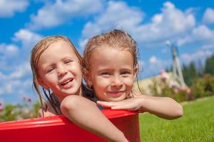 Due carino poco contento ragazze avendo divertimento nel piccolo piscina su il cortile all'aperto e godere vacanza foto