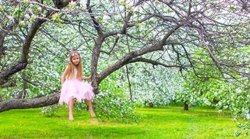 poco adorabile ragazza seduta su fioritura albero nel Mela giardino foto