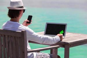 giovane uomo con tavoletta computer e cellula Telefono su tropicale spiaggia foto
