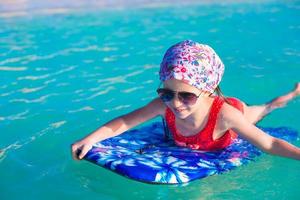 piccola ragazza adorabile su una tavola da surf nel mare turchese foto