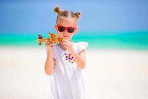 contento poco ragazza con giocattolo aereo nel mani su bianca sabbioso spiaggia. foto viaggio pubblicità, voli e le compagnie aeree