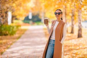 autunno concetto - bellissimo donna potabile caffè nel autunno parco sotto autunno fogliame foto