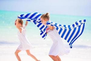 bambine che si divertono a correre con gli asciugamani sulla spiaggia tropicale con sabbia bianca e acqua turchese dell'oceano foto