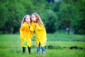 divertente carino bambino piccolo ragazze indossare impermeabile cappotto giocando all'aperto di piovoso e soleggiato giorno foto