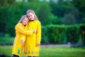 divertente carino bambino piccolo ragazze indossare impermeabile cappotto giocando all'aperto di piovoso e soleggiato giorno foto