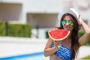 giovane donna nel cappello e occhiali da sole con anguria rilassante vicino piscina foto