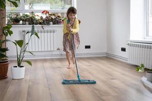 un' ragazza balli con un' Mocio per pulito il pavimento nel un' nuovo Casa - generale pulizia nel un vuoto camera, il gioia di in movimento, Aiuto con il lavori di casa foto