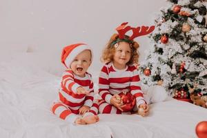 bambini nel rosso e bianca pigiama mangiare Natale dolci seduta nel letto. fratello e sorella, ragazzo e ragazza Condividere i regali. Natale mattina. stile di vita. spazio per testo. alto qualità foto